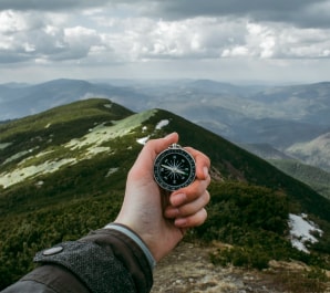 Рука, держащая компас перед горой.